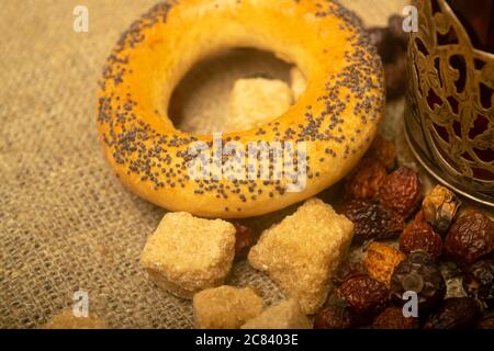 Piccoli bagel, pezzi di zucchero di canna e frutta secca di rosa canina sparsi su un panno di casa con una consistenza ruvida. Primo piano Foto Stock