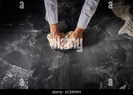 Chef pasticceria impastare un cumulo di pasta cruda per una panetteria o pizza base in una pizzeria italiana in un primo piano sulle sue mani su una superficie infarinata con copia Foto Stock