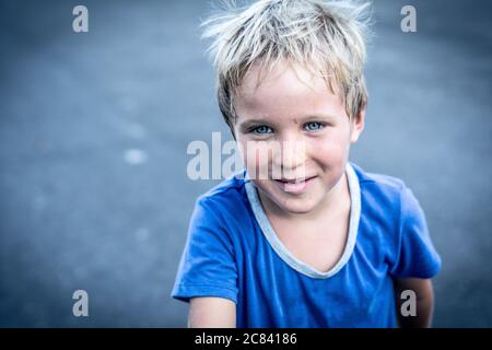 Ritratto di un divertente e felice mischievole allegro simpatico ragazzo biondo blu occhi facendo furti faccia sporca mentre si gioca, ridendo. Asilo, infanzia felice Foto Stock