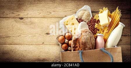Generi alimentari freschi e latticini in una borsa riutilizzabile che comprende formaggio, pasta, baguette, fagioli, uova e latte su legno con copyspace e visco Foto Stock