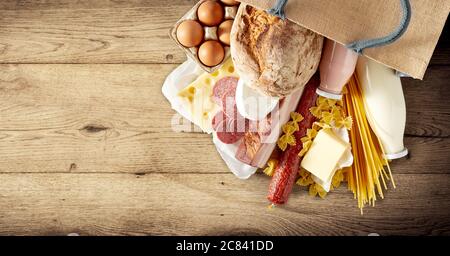 Borsa con pasta italiana secca e un assortimento di latticini, uova, salumi e salsiccia piccante su fondo rustico di legno con copyspac Foto Stock