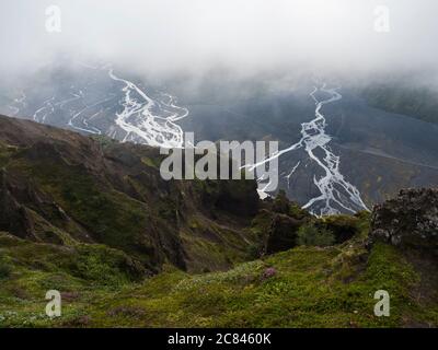 Vista dalla cima della montagna Valahnukur sul paesaggio della verde valle di Thorsmork con le rocce verdi affilate, il delta del fiume Krossa e la foresta verde. Nebbia Foto Stock