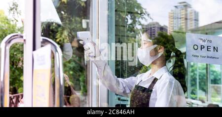 Cameriera asiatica con maschera faccia prendere la temperatura al cliente prima di entrare in ristorante. Ristorante nuovo stile di vita normale del ristorante dopo coro Foto Stock