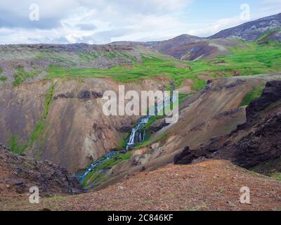 Valle di Reykjadalur con le sorgenti termali, prati verdi e rigogliosi, rocce e colline con vapore geotermico. Islanda del Sud vicino alla città di Hveragerdi. Estate Foto Stock