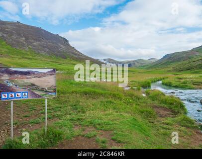 Islanda, Hveragerdi, 5 agosto 2019: Cartello di segnalazione turistica all'ingresso della valle di Reykjadalur con il fiume delle sorgenti calde, l'erba verde lussureggiante e. Foto Stock