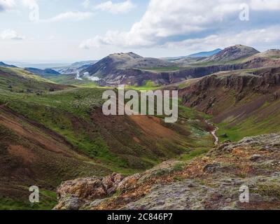 Valle di Reykjadalur con le sorgenti termali di fiume con prati verdi e colline con vapore geotermico. Islanda del Sud vicino alla città di Hveragerdi. Estate Foto Stock