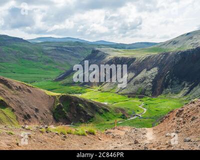 Valle di Reykjadalur con le sorgenti termali, prati verdi e rigogliosi, rocce e colline con vapore geotermico. Islanda del Sud vicino alla città di Hveragerdi. Estate Foto Stock