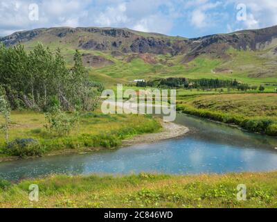 Idilliaco paesaggio di Hveragerdi vicino alla valle di Reykjadalur con le sorgenti termali di fiume, prati verdi e verdi lussureggianti prati e colline. Islanda del Sud. Estate mattina soleggiata Foto Stock
