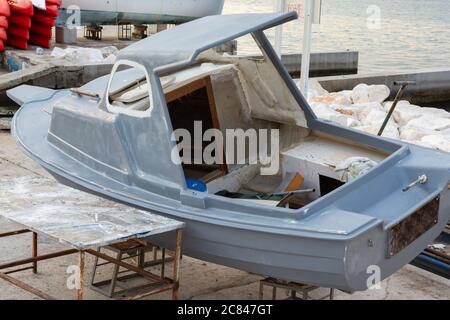 Una piccola barca è in fase di riparazione e di restauro in un ormeggia sulla riva prima di rientrare al mare Foto Stock