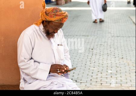 Mutrah, Oman - 10 febbraio 2020: Uomo adulto Omani in abbigliamento tradizionale con mobile in strada a Mutrah, Sultanato di Oman, Medio Oriente Foto Stock