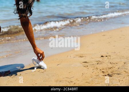 Donna che raccoglie i rifiuti in spiaggia, maschera facciale covid Foto Stock