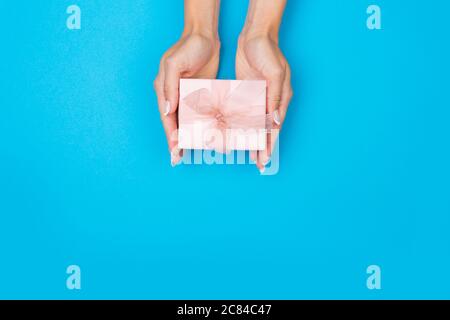 Mani che tengono carta regalo artigianale scatola con un regalo per Natale, Capodanno, San Valentino o anniversario su uno sfondo blu, vista dall'alto Foto Stock