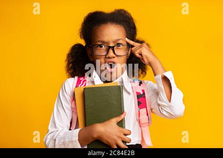 Dispiaciuto African School Girl Holding Libri su sfondo giallo, studio Foto Stock