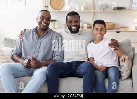 Ritratto di felice famiglia di uomini multigenerazionali neri che posano sul divano a casa Foto Stock