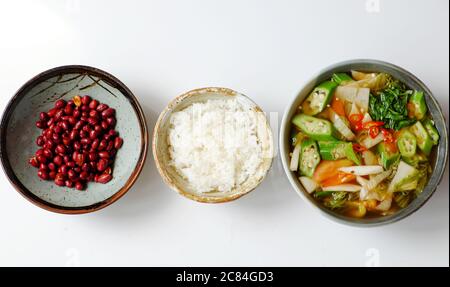 Vista dall'alto cucina vietnamita vegana, pasto giornaliero per famiglie su sfondo bianco, zuppa acida di verdure, arachidi fritte con salsa di soia e ciotola di riso per pranzo Foto Stock