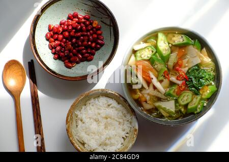 Vista dall'alto cucina vietnamita vegana, pasto giornaliero per famiglie su sfondo bianco, zuppa acida di verdure, arachidi fritte con salsa di soia e ciotola di riso per pranzo Foto Stock