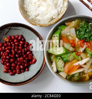 Vista dall'alto cucina vietnamita vegana, pasto giornaliero per famiglie su sfondo bianco, zuppa acida di verdure, arachidi fritte con salsa di soia e ciotola di riso per pranzo Foto Stock