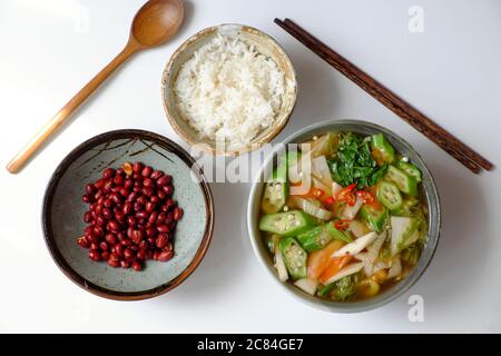 Vista dall'alto cucina vietnamita vegana, pasto giornaliero per famiglie su sfondo bianco, zuppa acida di verdure, arachidi fritte con salsa di soia e ciotola di riso per pranzo Foto Stock