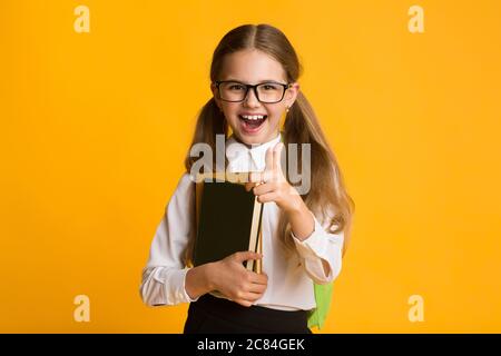 Nerdy Schoolgirl punta la dito sorridendo al posizionamento della fotocamera, Studio Shot Foto Stock