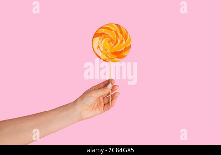 Millennial girl che tiene yummy swirl lollipop su sfondo rosa, primo piano di mano Foto Stock