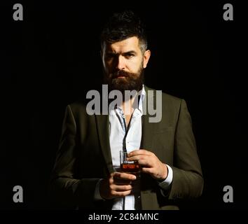 Uomo d'affari con barba e bevande su sfondo nero. Concetto di alcol e bevande. Intenditore con cognac o brandy elegante look bevande. Uomo con viso meditato in tuta con bicchiere di alcol. Foto Stock