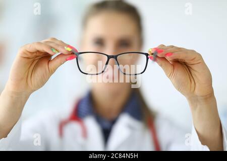 Donna medico che tiene gli occhiali nel suo closeup mani Foto Stock