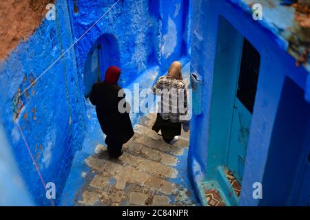 Marocco, Chefchaouen : Donne anziane con veli che scendono le scale in un vicolo della Città Vecchia. Case con pareti blu Foto Stock