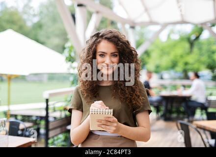 Ritratto di cameriera in piedi sulla terrazza ristorante, tenendo ordine pad. Foto Stock