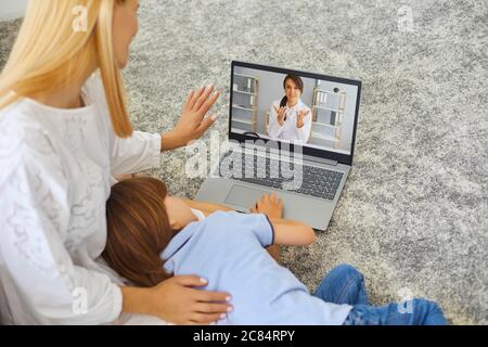 Giovane madre e bambino malato usando il servizio medico in linea a casa, consultando il pediatra con video chat Foto Stock