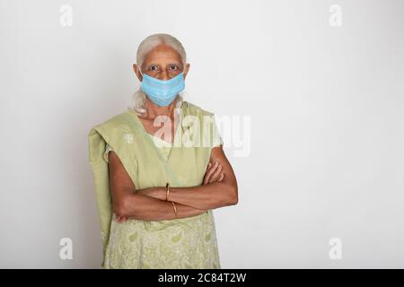 Donna indiana matura che indossa maschera di protezione Covid, nonna indiana che leviga con le braccia incrociate Foto Stock