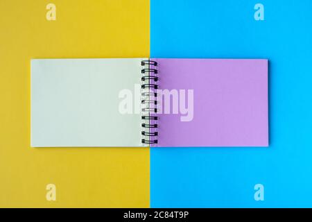 Un notebook con pagine multicolore si trova su uno sfondo giallo e blu. Vista dall'alto, disposizione piatta, spazio per il testo. Foto Stock