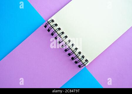 Un notebook con pagine multicolore si trova su uno sfondo rosa e blu. Vista dall'alto, disposizione piatta, spazio per il testo. Foto Stock