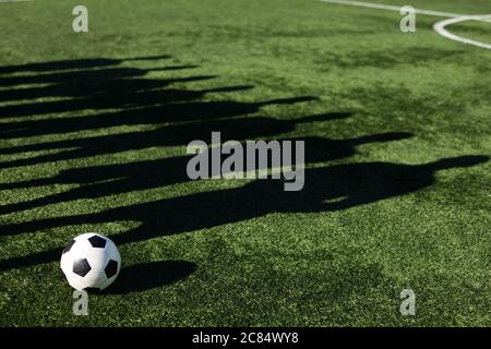 Ombra sul campo di erba di un gruppo di giocatori di calcio maschili che si allenano in un campo sportivo al sole, in piedi accanto a loro palla. Foto Stock