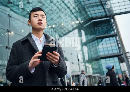 Giovane uomo d'affari di stile con smartphone che attende con attenzione vicino all'aeroporto Foto Stock