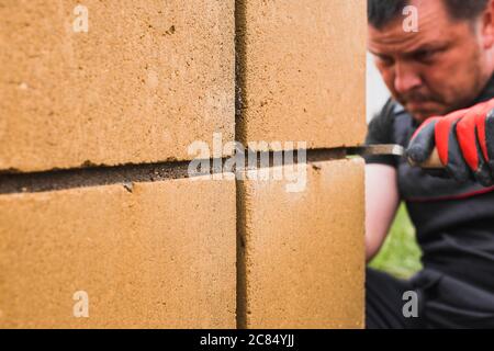 Mani di un muratore professionale con guanti mentre si lavora sulla costruzione di pareti in pietra - un cazzuola per l'applicazione di Malta in muratura e un martello per muratura Foto Stock