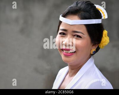 La donna balinese indonesiana matura indossa abiti bianchi e sorride per la macchina fotografica durante una cerimonia religiosa indù tempio (Odalan festival). Foto Stock