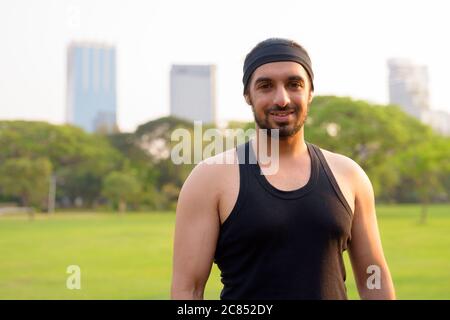 Felice giovane bell'uomo indiano sopportato sorridente al parco Foto Stock