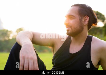 Vista del profilo di un giovane bell'uomo indiano seduto al parco Foto Stock