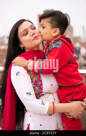 Felice figlio carino baciando sua madre su guance. È in piedi vicino alla ringhiera sul tetto e passare il tempo libero con suo figlio. Foto Stock