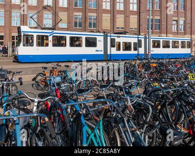 Amsterdam, Paesi Bassi - Ottobre 15 2018: Un tram passa in bicicletta parcheggiata vicino alla stazione centrale di Amsterdam in un pomeriggio soleggiato. Foto Stock