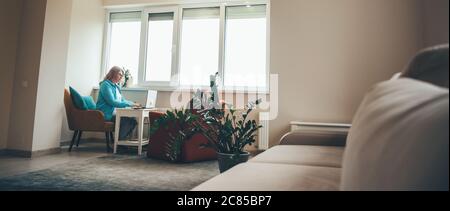Bionda donna anziana che lavora a distanza da casa sul laptop durante il blocco Foto Stock