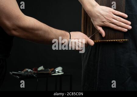 Forbici da parrucchiere con pettine e ciocca di capelli brunette su fondo nero Foto Stock