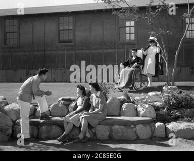 Nurse Aiko Hamaguchi con il paziente Tom Kano, giovane uomo che parla con le giovani donne sedute sul banco di pietra in primo piano, Centro di rilocazione, Manzanar, California, USA, Ansel Adams, Manzanar War Relocation Center Photographs, 1943 Foto Stock