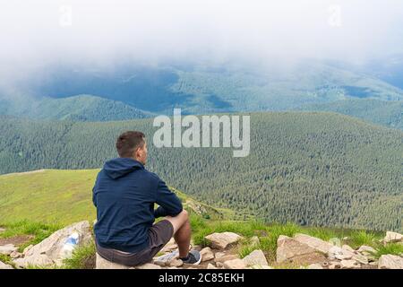 Vista laterale giovane uomo escursionista seduto sulla cima della montagna`s godendo di rocce sfondo paesaggio. Viaggi stile di vita wanderlus Foto Stock
