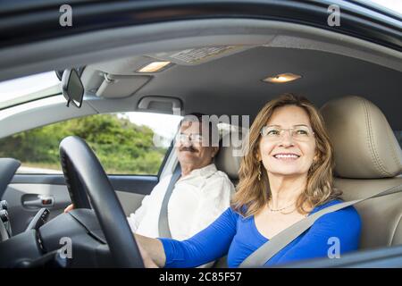 Primo piano di una coppia ispanica di mezza età che sorride in un auto con la moglie che guida Foto Stock