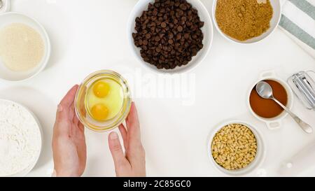 Ricetta di biscotti al cioccolato. I trucioli di cioccolato, lo zucchero di canna, le noci, le uova e alcuni altri ingredienti per cucinare hanno bisogno di primo piano su tavola bianca della cucina Foto Stock