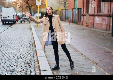 Bella ragazza elegante in trench cappotto cercando di prendere un taxi sulla strada Foto Stock