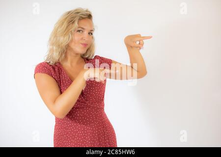 Bella donna bionda sorridente in un vestito rosso che indica qualcosa Foto Stock