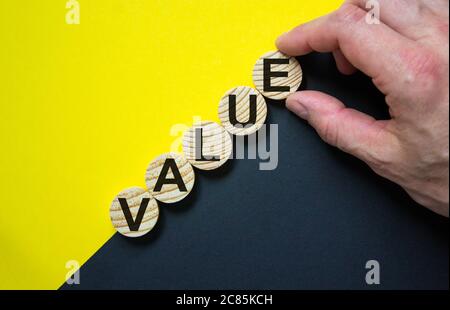 Cerchi di legno con la parola 'valore' impilata come scala su carta sfondo giallo e nero, spazio di copia. Mano maschio. Processo di successo del concetto aziendale. Foto Stock