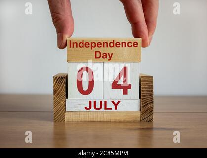 La mano maschile mette un blocco con l'iscrizione 'Independence Day' su cubi con la data del 04 luglio. Tavolo di legno. Splendido sfondo bianco, spazio per la copia. Foto Stock